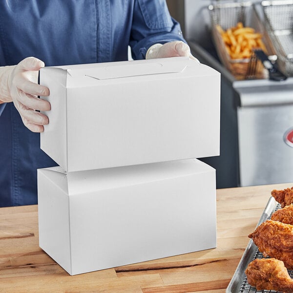 A person wearing gloves holding a Southern Champion white barn box filled with food.