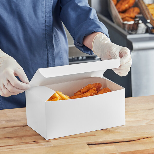 A person in gloves opening a Southern Champion white take-out box of food.