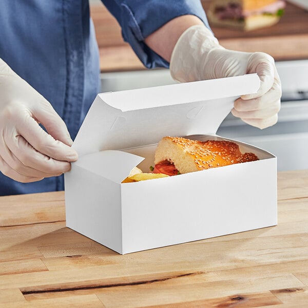 A person in gloves is putting food into a white Southern Champion lunch box.