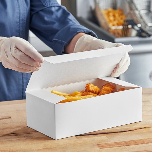 A person in gloves opening a white take-out box of chicken and fries.