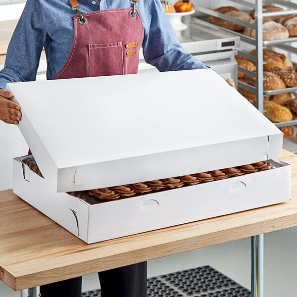 A person wearing a red apron holding a white Southern Champion full sheet cake box.