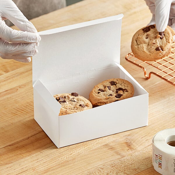 A gloved hand puts a chocolate chip cookie in a white Southern Champion bakery box.