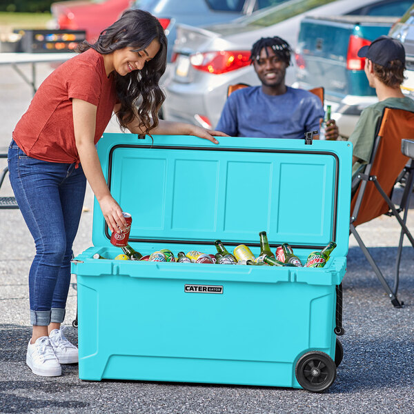 A woman in a blue shirt putting a drink into a CaterGator outdoor cooler next to a man wearing a black hat.