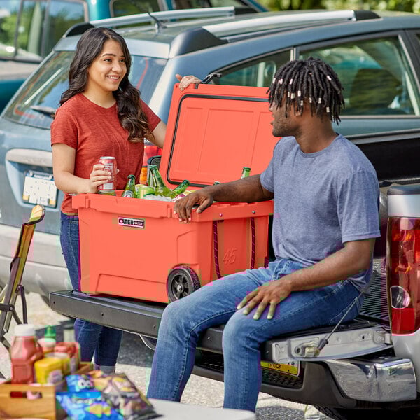 A man and woman sitting on the back of a truck with a CaterGator outdoor cooler.