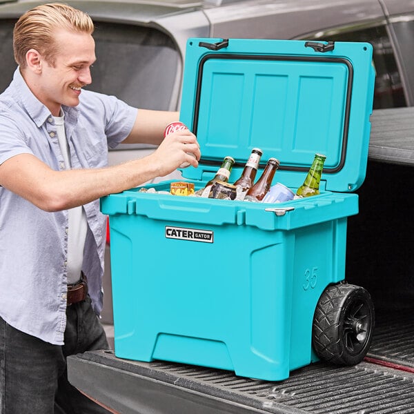 A man opening a CaterGator outdoor cooler and putting bottles inside.