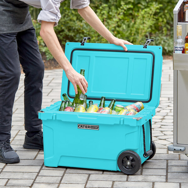 A man holding a CaterGator Sky Blue outdoor cooler filled with beer bottles and cans.