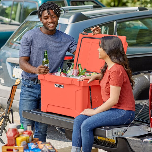 A man and woman sitting on the back of a truck with a CaterGator cooler.