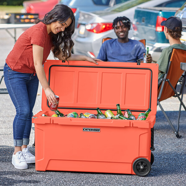 A woman putting a can into a CaterGator outdoor cooler filled with ice.