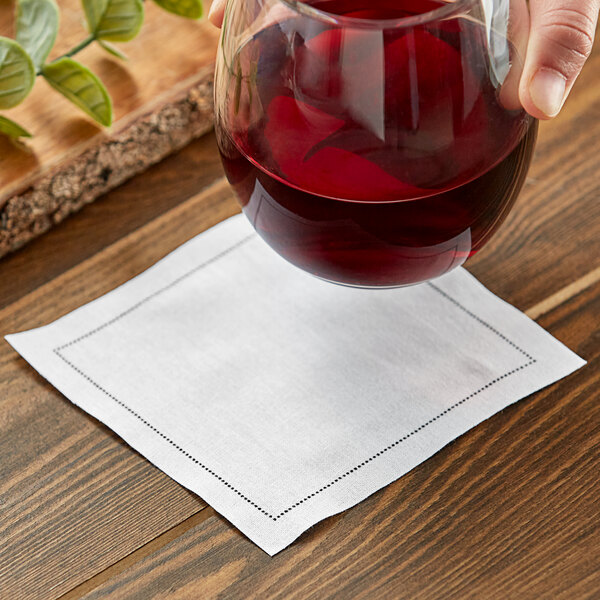 A hand holding a glass of red wine over a white cotton cloth napkin.