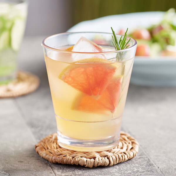 An Acopa stackable rocks glass of orange juice with ice, orange slices, and a rosemary leaf.