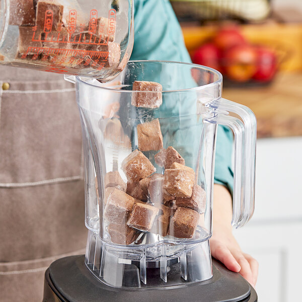 A person pouring brown cubes into a blender.