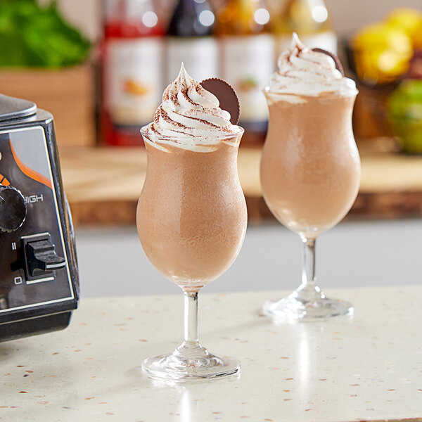 Two glasses of chocolate peanut butter smoothies topped with whipped cream on a counter.