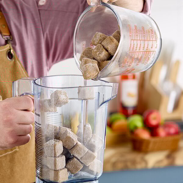 A person pouring brown sugar into a blender filled with brown cubes.
