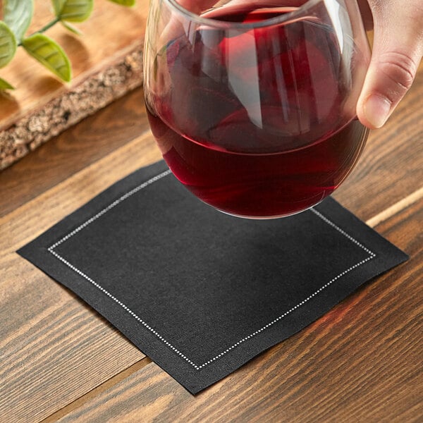 A hand holding a glass of red wine over a black Choice cloth napkin.
