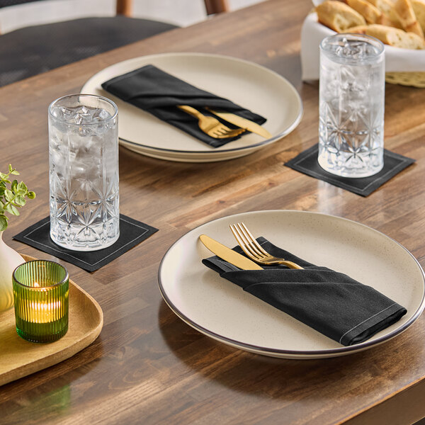 A set of black single-use cotton beverage napkins placed under glasses of water on a dining table.