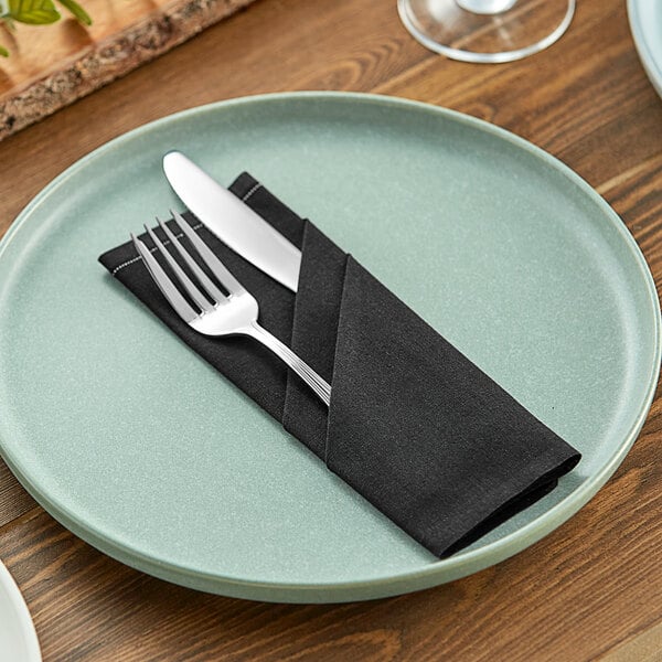 A black cloth napkin with a fork and knife on a plate.