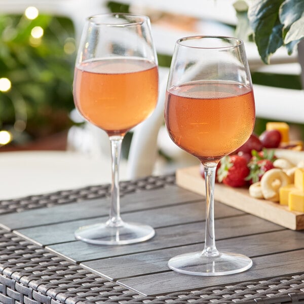 Two Acopa Endure Tritan plastic wine glasses on a table with wine, fruit, and cheese on an outdoor patio.