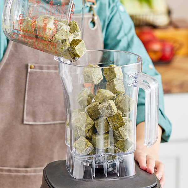 A person pouring green cubes into a blender.