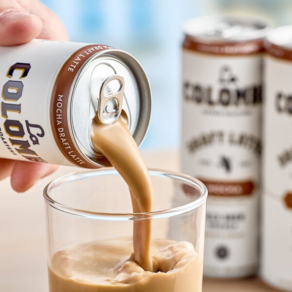 A hand pours La Colombe Mocha Draft Latte into a glass.