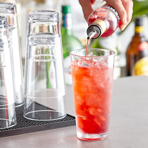 A person pouring a red drink from a bottle into an Acopa Tritan plastic cooler glass filled with ice.