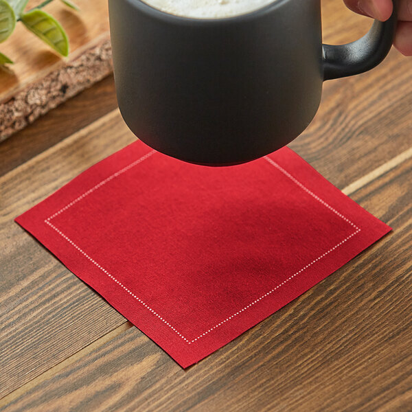 A hand holding a black mug with white foam over a red Choice cloth napkin.