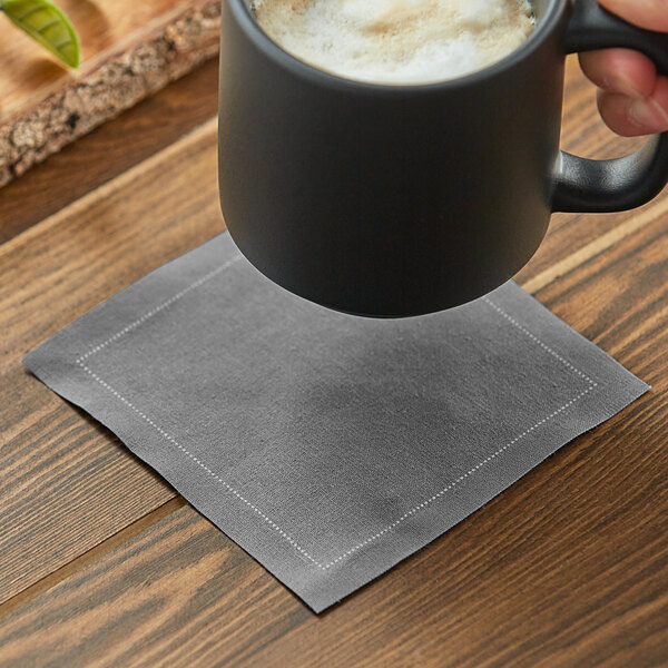 A hand holding a black mug with foam above a gray Choice cloth napkin.