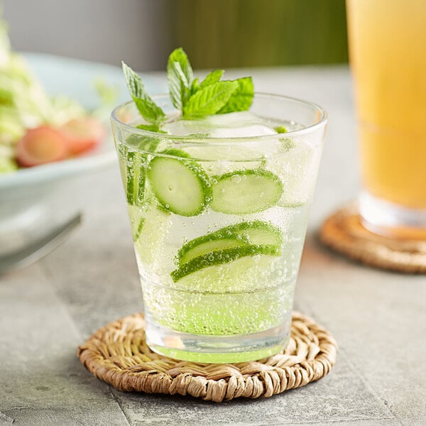 An Acopa Tritan plastic stackable rocks glass with cucumber and mint in water and a glass of lemonade.