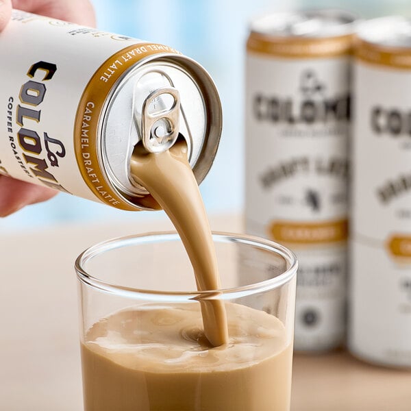 A hand pours La Colombe Caramel Draft Latte into a glass.