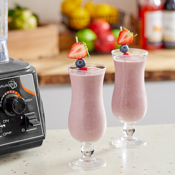 Two glasses of pink smoothies with strawberries and blueberries sitting on a counter.