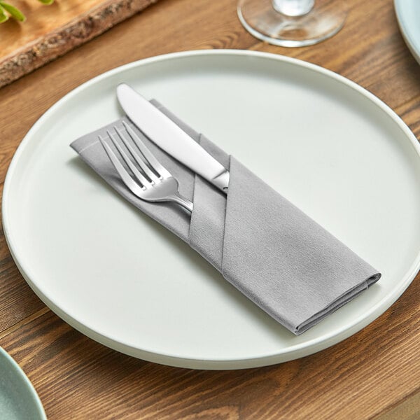 A plate with a fork and knife wrapped in a Choice gray cotton napkin.