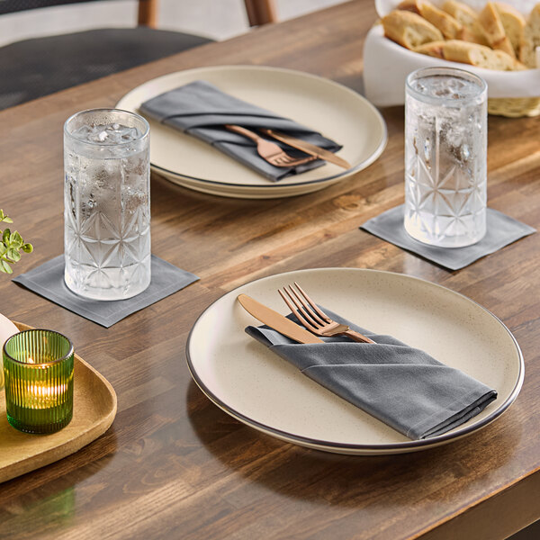 A set of gray single-use cotton dinner napkins placed on plates and under glasses on a dining table.