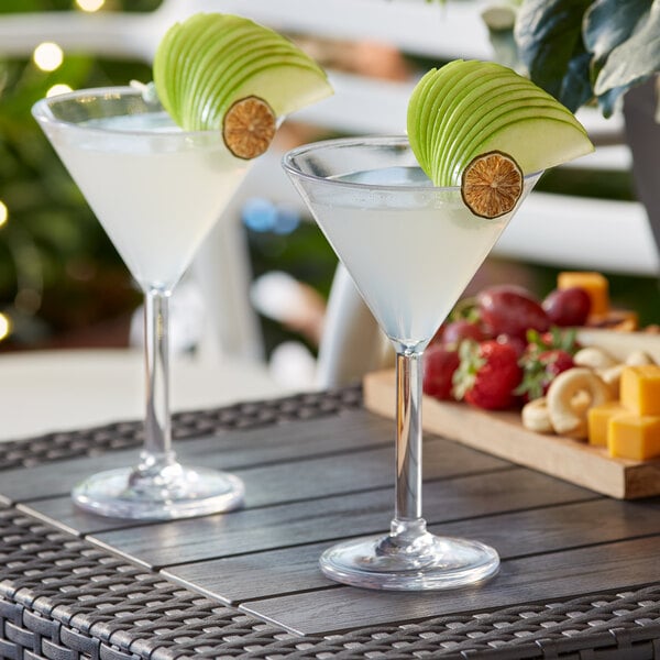 Two Acopa Endure Tritan plastic martini glasses on a table with liquid and fruit.