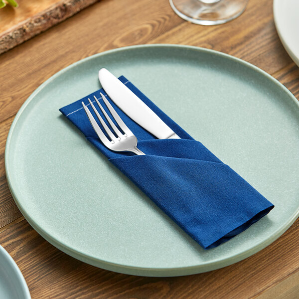 A navy blue cloth napkin with a fork and knife on a plate.
