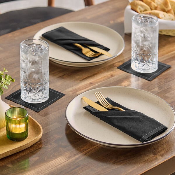A set of black single-use cotton dinner napkins placed on plates at a dining table.