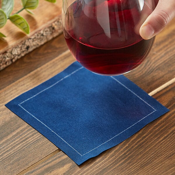 A hand holding a glass of red liquid over a navy blue cloth napkin.