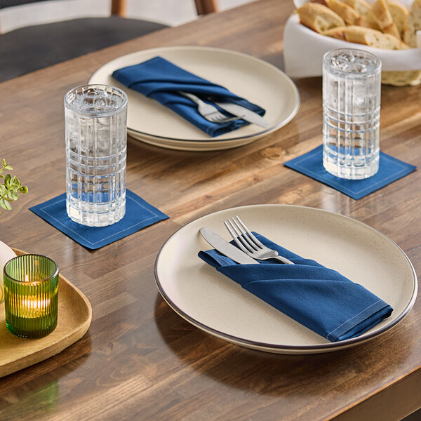 A navy blue single-use cotton beverage napkin placed under a glass of water on a dining table.