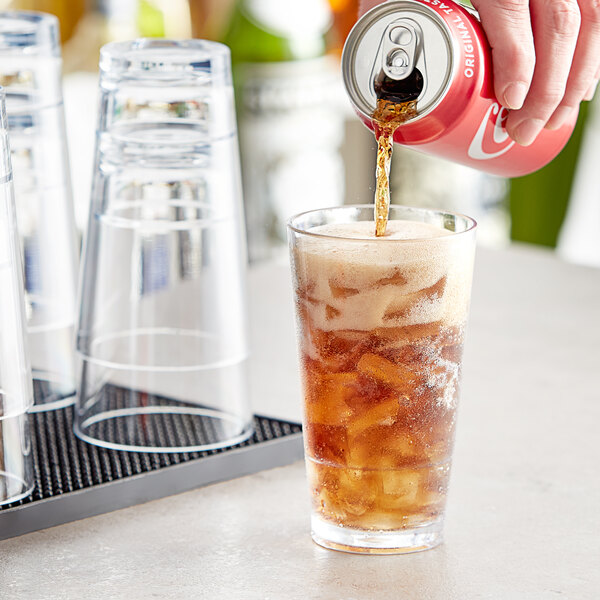 A hand pouring soda into an Acopa Endure highball glass of brown liquid with ice.