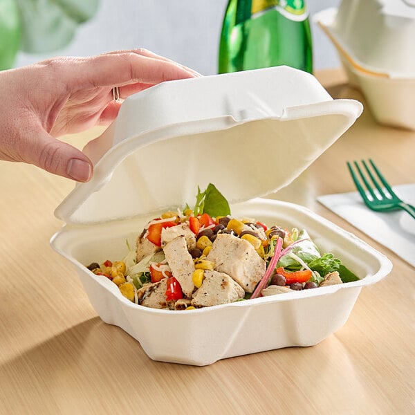 A hand holding a salad in a Fabri-Kal Greenware hinged container.