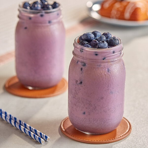 Two jars of purple smoothies with blueberries and a straw.