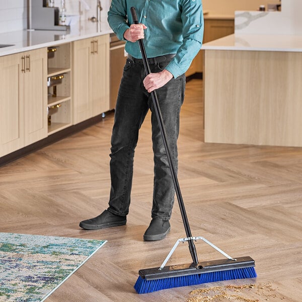 A man using a Lavex Polypropylene Push Broom with a squeegee attachment and metal handle to sweep a floor in a professional kitchen.