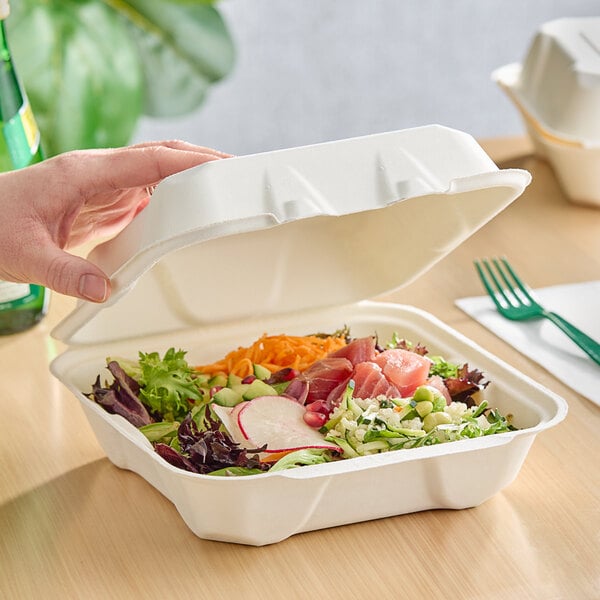 A hand holding a white Fabri-Kal Greenware hinged container of salad.