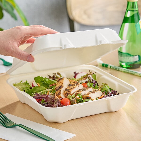 A hand holding a white Fabri-Kal Greenware hinged container of food.