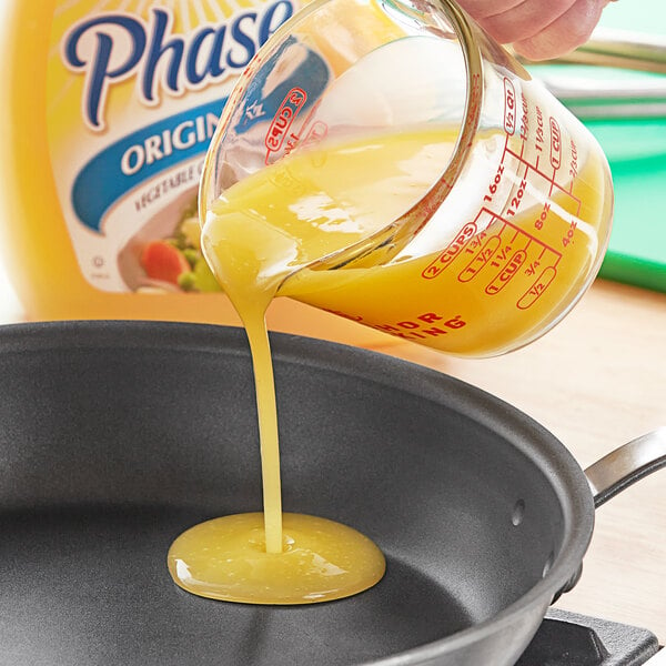 A person pouring Phase butter-flavored oil into a frying pan.