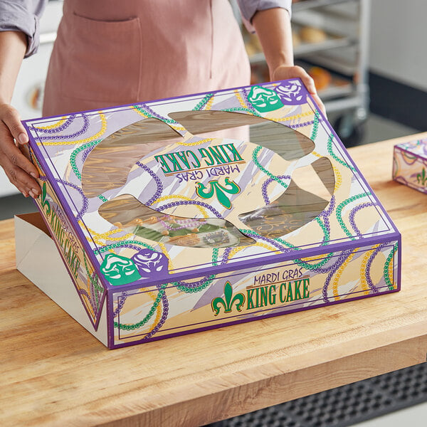 A woman holding a Southern Champion bakery box with a Mardi Gras King Cake design.