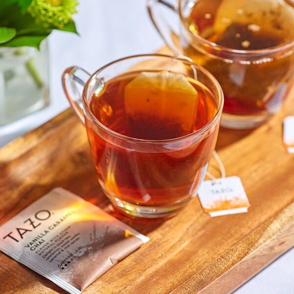 A wooden tray with two cups of Tazo Vanilla Caramel Chai tea and a tea bag.