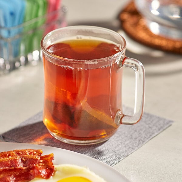 A plate with bacon and eggs and a box of PG Tips black tea on a table with a glass mug of tea.