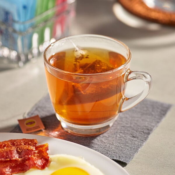 A plate of bacon and eggs and a cup of Lipton Peach Mango black tea on a table.