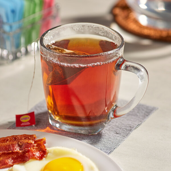 A plate with bacon and eggs and a box of Lipton English Breakfast Pyramid tea bags on a table.