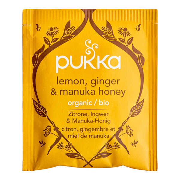 A yellow Pukka Organic Lemon, Ginger, and Manuka Honey Tea package on a table.