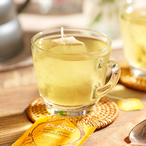A glass cup of Pukka Organic Lemon, Ginger, and Manuka Honey tea with a tea bag in it.